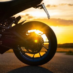 Sport motorbike rear wheel with perforated disc brake and chain drive silhouetted against a golden sunset on open asphalt road